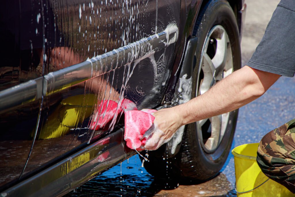 Man washes car wheel. Male hand holds pink sponge with soapy foam for cleaning.