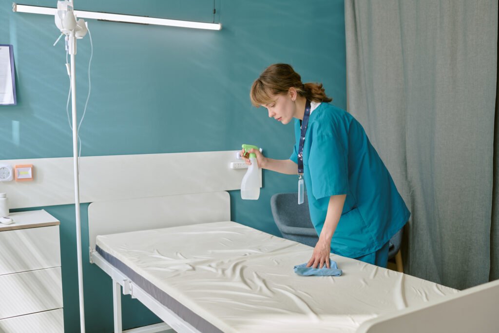 Caucasian Young Adult Woman Cleaning Hospital Bed with Disinfectant Spray