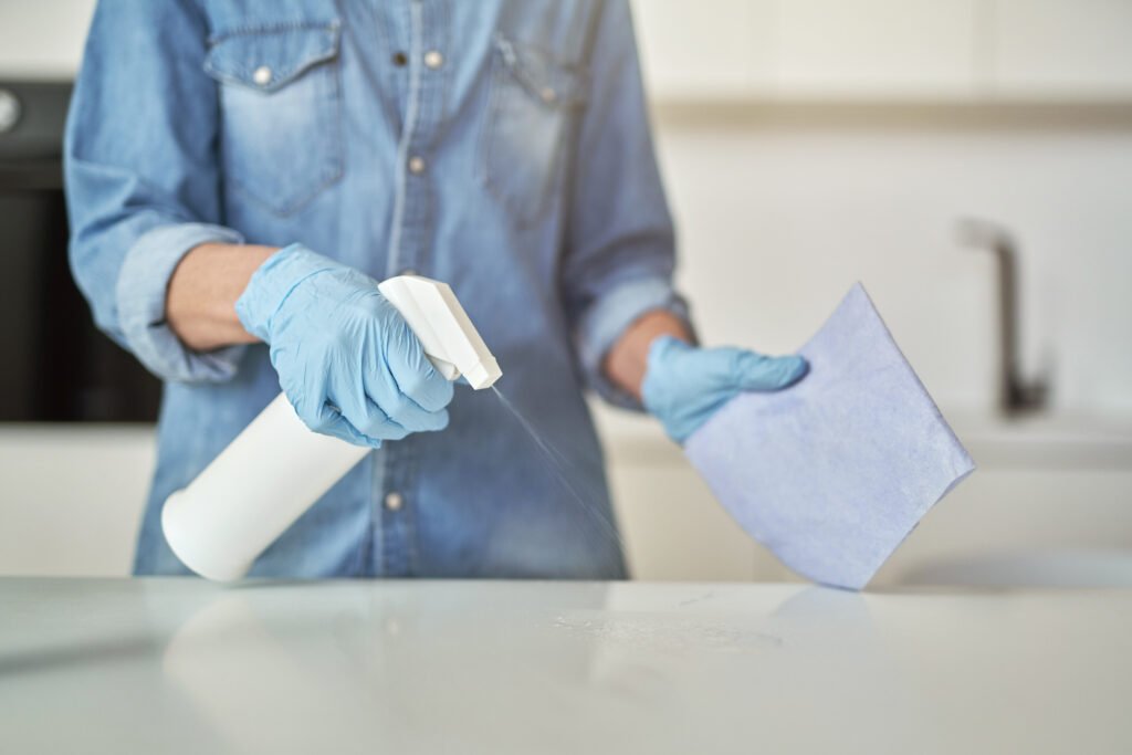 Close up shot of female hands in rubber gloves using detergent spray and cloth while cleaning kitchen surface